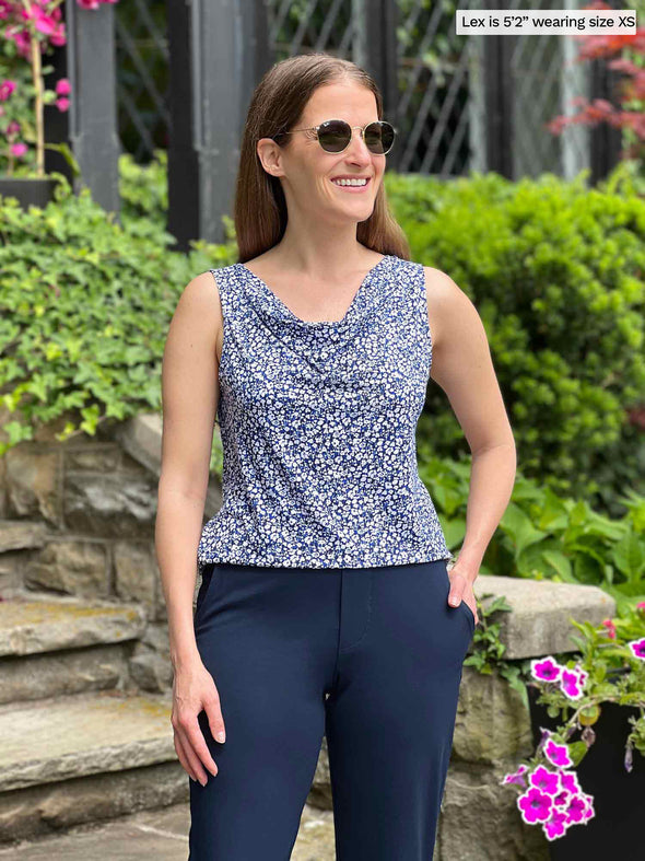 Miik model Lex (5'2", xsmall) smiling and looking away wearing Miik's Ada reversible draped cowl neck tank in baby's breath with a navy pant and sunglasses 