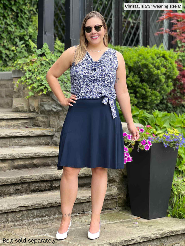 Miik model Christal (5'3", medium) smiling wearing Miik's Ada reversible draped cowl neck tank in baby's breath print along with a Blair belt in the same matching print and a flouncy skirt in navy