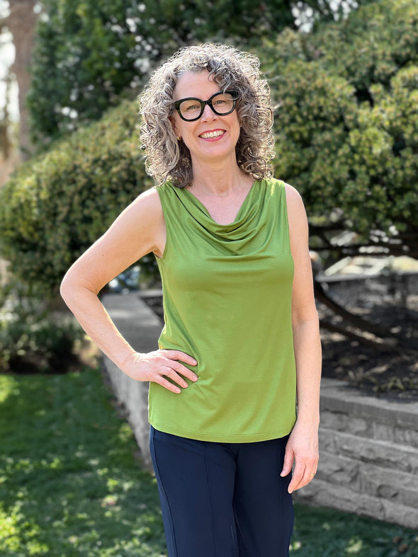 Miik model Liane (5'9", small) smiling wearing a navy dress pant along with Miik's Ada reversible draped cowl neck tank in green moss #color_moss 