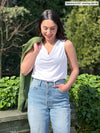 Woman standing in front of nature wearing Miik's Ada reversible draped cowl neck tank in white with jeans.