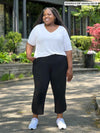 Miik model plus size Kimesha (5'8", 3x) smiling and looking away wearing a white v-neck tee with Miik's Akira tulip hem capri pant in black #color_black