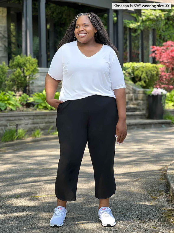 Miik model plus size Kimesha (5'8", 3x) smiling and looking away wearing a white v-neck tee with Miik's Akira tulip hem capri pant in black #color_black