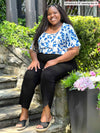 Miik model plus size Kimesha (5'8", 3x) sitting and smiling wearing Miik's Akira tulip hem capri pant in black with a top in ink leaf print #color_black