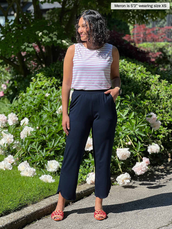 Woman standing in front of a garden wearing Miik's Akira tulip hem capri pant in navy with a white and pink stripe tank. #color_navy