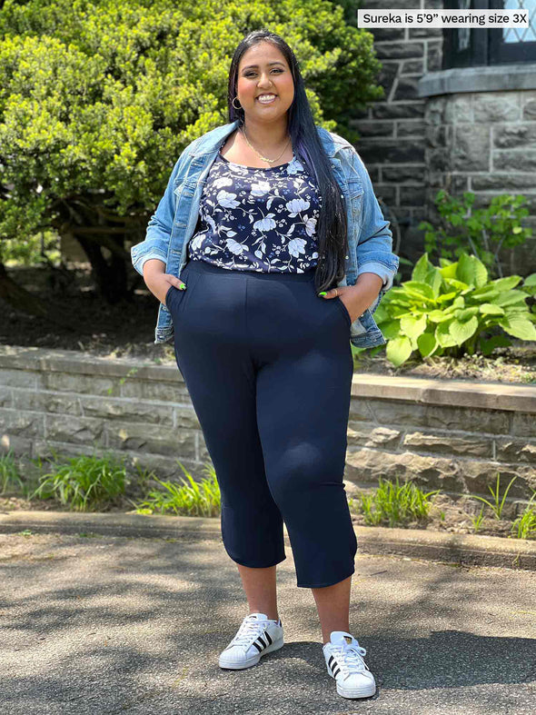 Miik model plus size Sureka (5'9", 3x) smiling wearing Miik's Akira tulip hem capri pant in navy with a printed floral tee tucked in and a denim jacket #color_navy