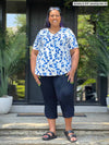 Miik model Sureka (5'9", 3x) smiling wearing Miik's Akira tulip hem capri pant in navy with a ink leaf top #color_navy