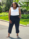 Miik model plus size Kimesha (5'8", 3x) smiling wearing Miik's Akira tulip hem capri pant in navy with a white tank top tucked in #color_navy