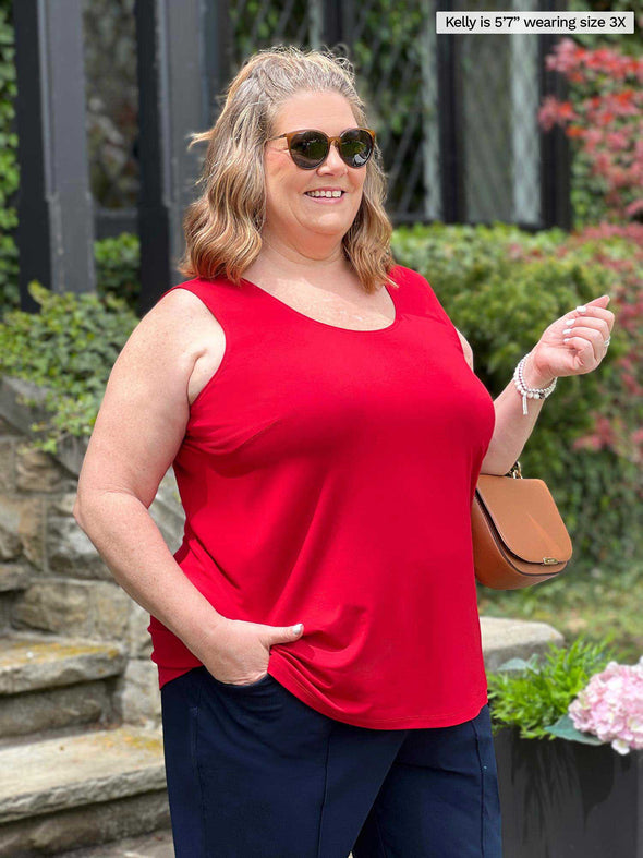Miik model plus size Kelly (5'7", 3x) smiling while standing sideway wearing Miik's Alanis relaxed tank top in poppy red with a navy pant and sunglasses 