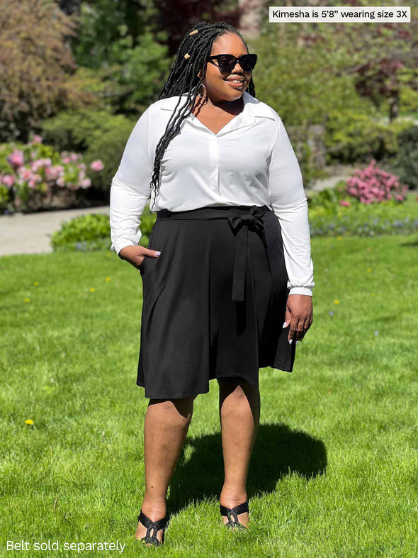 Miik model Kimesha (5'8", 3x) smiling and looking away wearing a collared shirt in white with Miik's Alara pocket swing skirt in black with a matching colour belt 