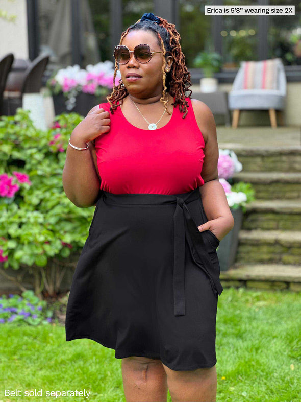 Miik model plus size Erica (5'8", 2x) looking away wearing Miik's Alara pocket swing skirt in black with a matching colour belt and a tank top in poppy red and sunglasses 