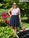 Woman standing in nature wearing Miik's Alara pocket swing skirt in navy with a white and pink stripe tank.