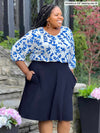 Miik model plus size Kimesha (5'8", 3x) smiling while standing sideway wearing Miik's Alara pocket swing skirt in navy with a ink leaf blouse tucked in