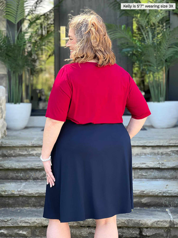 Miik model plus size Kelly (5’7”, 3x) standing with her back towards the camera showing the back of Miik's Alara pocket swing skirt