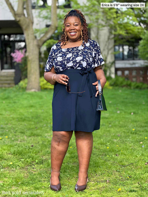 Miik model plus size Erica (5'8", 2x) smiling wearing Miik's Alara pocket swing skirt in navy with a matching colour belt and a floral tee 
