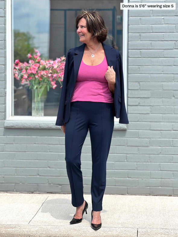 Miik founder Donna (5'6, small) smiling and looking away wearing Miik's Amina reversible shelf bra tank in pretty in pink with a navy dress pant and a matching colour blazer over the shoulders