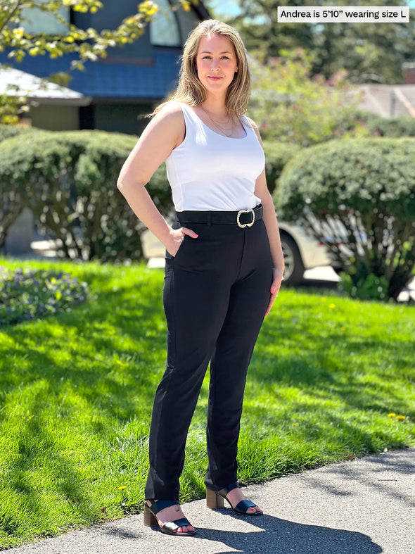 Miik model Andrea (5'10", large) smiling wearing a dress pant in black with Miik's Amina reversible tank shelf bra in white and a black belt 
#color_white
