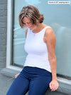 Miik founder Donna (5'6", small) leaning against to a window and looking down wearing Miik's Amina reversible tank shelf bra in white with a navy dress pant 
#color_white 