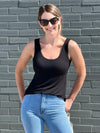 Miik model Jo (5'6", xsmall) smiling while standing in front of a brick wall wearing Miik's Amina reversible tank shelf bra in black with jeans and sunglasses 
#color_black 