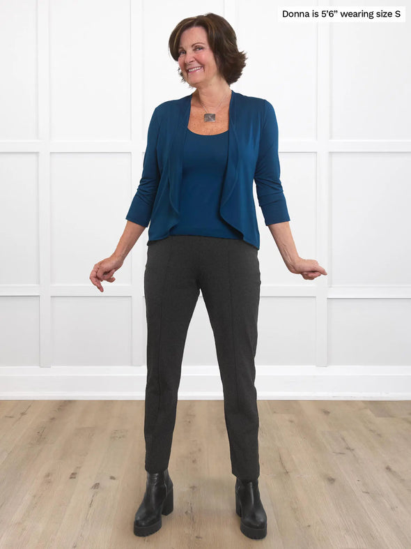 Miik founder Donna (5'6", small) smiling while standing in front of a white wall wearing Miik's Amina reversible tank shelf bra in teal with a matching cropped cardigan and a charcoal dress pant and boots 
#color_teal 