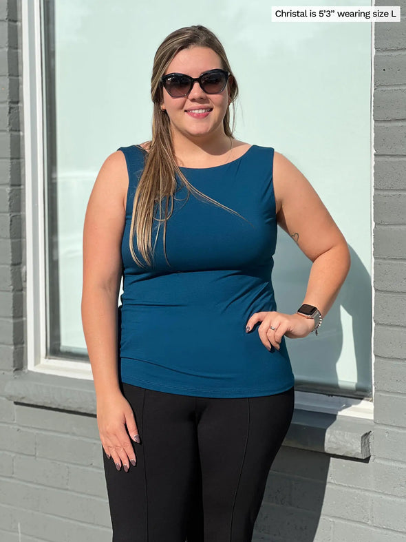 Miik model Christal (5'3", large) smiling while standing in front of a window wearing Miik's Amina reversible tank shelf bra in teal with a black dress pant and sunglasses 
#color_teal 