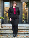 Miik model Bri (5'5", xlarge) smiling and looking away wearing a black dress pant, a cerise top and Miik's Anne soft stretch blazer in black #color_black 