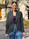 Miik model Meron (5'3", xsmall) smiling wearing Miik's Anne soft stretch blazer in charcoal with a port tank top and jeans #color_port 