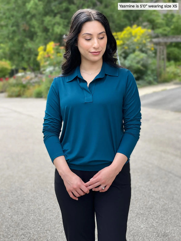 Miik model Yasmine (5'0", xsmall, petite) smiling and looking down wearing Miik's Arianna collared shirt in teal with a navy pant #color_teal 