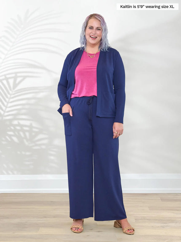 Miik model Kaitlin (5'9", XL/XXL) smiling wearing a pink tank top along with Miik's Arlon cardigan with pockets in marine blue with pants in the same colour #color_marine-blue