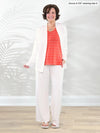 Miik founder Donna (5'6", small) smiling while standing in front of a white wall wearing Miik's Arlon cardigan with pockets in natural with a pant in the same matching colour and a papaya pinstripe tank top #color_natural