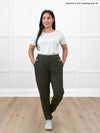 Miik model Yasmine (5'0", xsmall) smiling and looking away wearing a white tee tucked in Miik's Ashton patch pocket jogger in olive #color_olive 