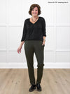 Miik founder Donna (5'6", small) smiling while standing in front of a white wall wearing Miik's Ashton patch pocket jogger in olive with a black blouse #color_olive 