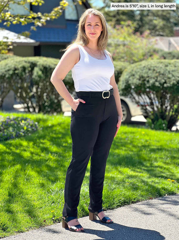 Miik model Andrea (5'10", large) wearing Miik's Asia mid-rise slim pant in black, long length, with a belt and a white tank top #color_black 