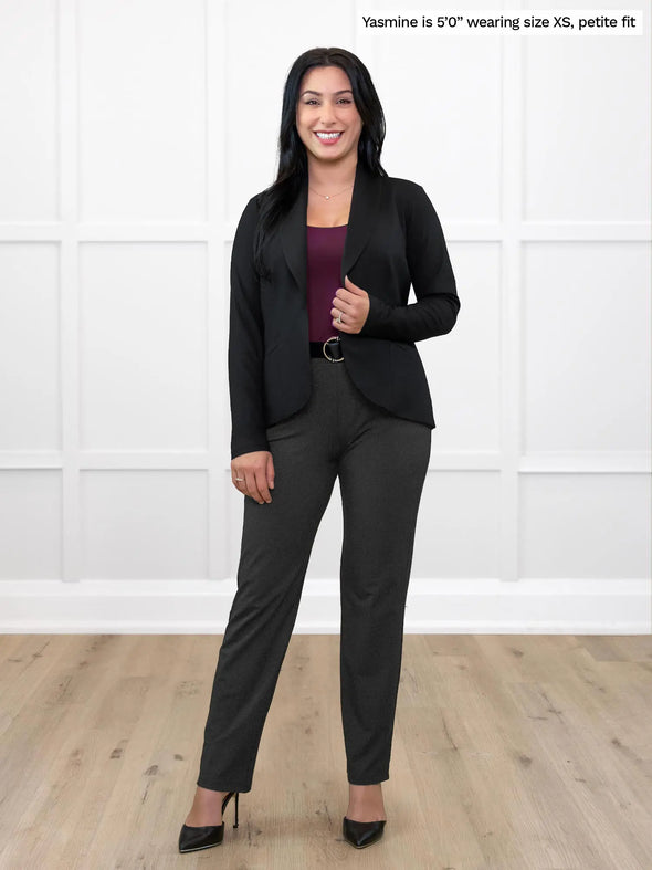 Miik model Yasmine (5'0", xsmall) standing in front of a white wall smiling wearing Miik's Asia mid-rise slim pant in charcoal, petite fit, with a black blazer and port top #color_charcoal