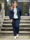 Miik model Bri (5'5", xlarge) smiling and looking down wearing Miik's Asia mid-rise slim pant in navy, regular fit, with a soft blazer in the same colour and a water lily tee #color_navy