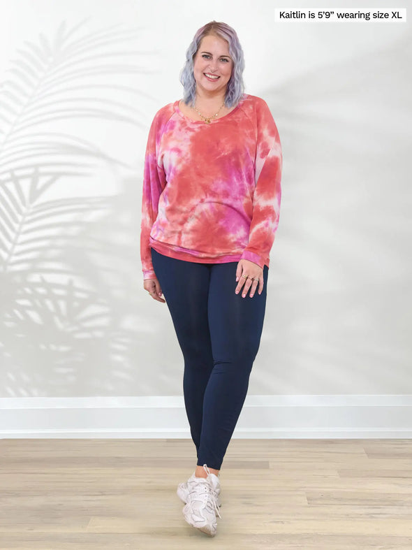 Miik model Kaitlin (5'9", XL/XXL) smiling wearing a navy legging pant with Miik's Aurelia lightweight french terry sweatshirt in coral reef #color_coral-reef