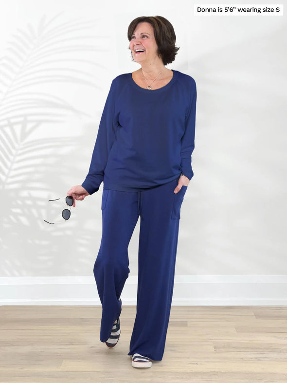 Miik founder Donna (5'6", small) smiling and looking away wearing Miik's Aurelia lightweight french terry sweatshirt in marine with a wide leg pant in the same matching colour #color_marine-blue