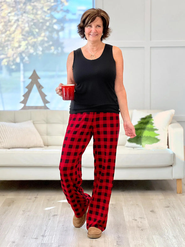 Miik founder Donna (5'6", small) smiling wearing Miik's Bryce plaid bamboo PJ pant in poppy buffalo plaid with a black tank top while holding a red mug #color_poppy-buffalo-plaid