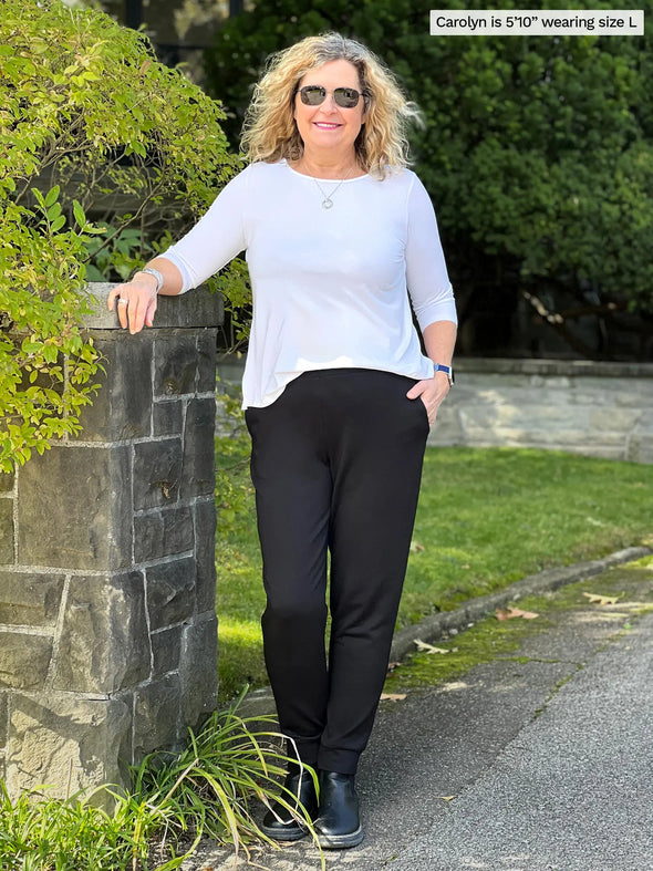 Miik model Carolyn (5'10", large) smiling wearing Miik's Cameron luxe fleece jogger with pockets in black with a 3/4 sleeve top in white #color_black