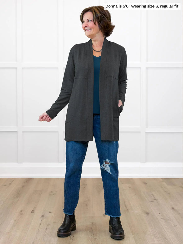 Miik founder Donna (5'6", small) smiling and looking away wearing Miik's Carmen luxe fleece cardigan with pockets in charcoal, regular fit, with a teal v-neck tee and ripped jeans #color_charcoal