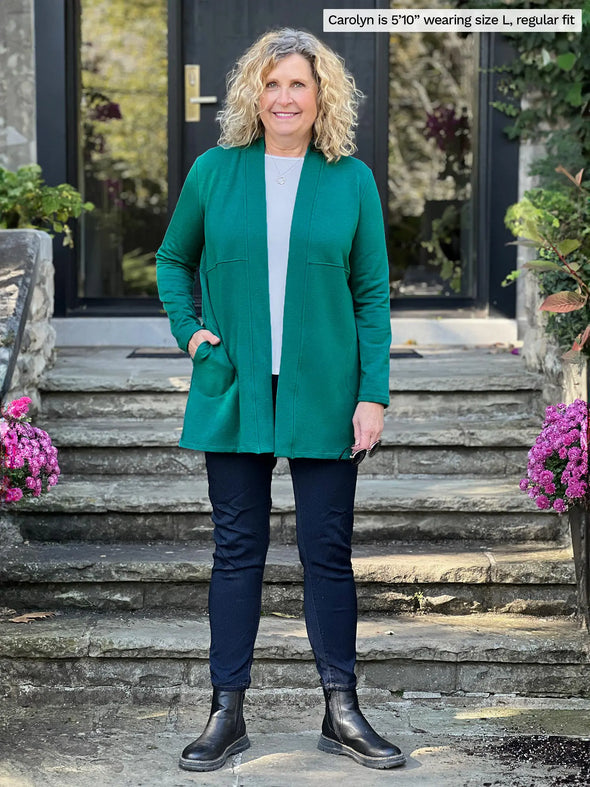 Miik model Carolyn (5'10", large) smiling wearing Miik's Carmen luxe fleece cardigan with pockets in jade melange, regular fit, with a white tee, jeans and boots #color_jade-melange