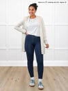 Miik model Meron (5'3", xsmall) smiling and looking away while standing in front of a white wall wearing Miik's Carmen luxe fleece cardigan with pockets in oatmeal melange, regular fit, with a white tee, navy leggings and sneakers #color_oatmeal-melange 