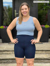 Miik model Christal (5'3", medium) smiling wearing Miik's Chalha high waisted mid thigh biker short in navy with a blue stripe tank top 