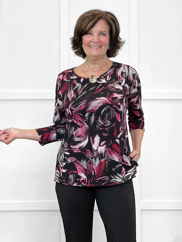 Miik founder Donna (5'6", small) smiling wearing Miik's Chris 3/4 sleeve scoop neck top in midnight floral with a black dress pant 