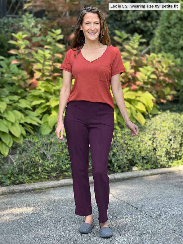 Miik model Lex (5'2", xsmall) smiling wearing Miik's Christal pull-on pintuck ankle pant in port, petite fit, along with a v-neck t shirt with pockets in paprika melange 
#color_port 