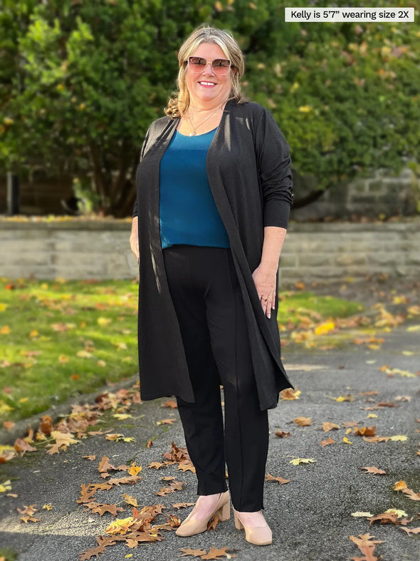 Miik model Kelly (5'7", 2x) smiling wearing Miik's Christal pull-on pintuck ankle pant in black, a charcoal duster cardigan and a teal tank top #color_black