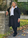 Miik model Kimesha (5'8", 3x) smiling wearing Miik's Christal pull-on pintuck ankle pant in black with a duster cardigan in the same colour and a collared white shirt #color_black