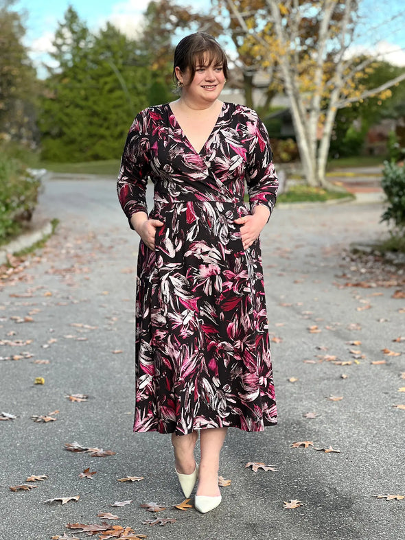 Miik model Bri (5'5", xlarge) smiling with both hands on pockets wearing Miik's Claudine tie waist midi dress in midnight floral print