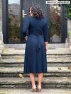 Miik model Meron (5’3”, xsmall) standing with her back towards the camera showing the back of Miik's Claudine tie waist midi dress in navy #color_navy