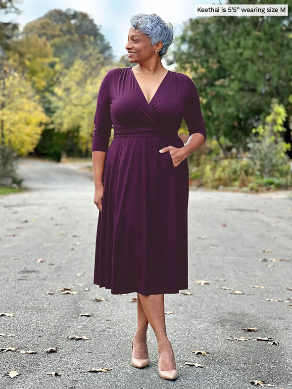 Miik model Keethai (5'5", medium) smiling and looking away wearing Miik's Claudine tie waist midi dress in port #color_port 