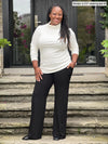 Miik model Marilyn (5'2", medium) smiling wearing a wide leg pant with pockets along with Miik's Cora ribbed turtleneck top in natural #color_natural 